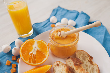 Serving table for breakfast: orange juice, fresh bread, honey with orange zest.