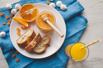 Serving table for breakfast: orange juice, fresh bread, honey with orange zest.
