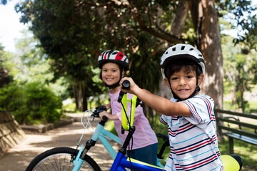 Portrait of smiling children standing with bicycle in park