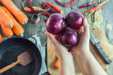 female hands holding three red onions on the background of the t