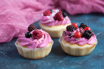 Homemade vanilla cupcakes with multicolor cream cap and berries on a dark blue background.