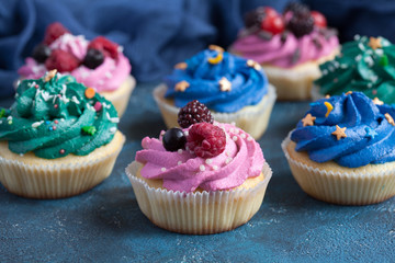 Homemade vanilla cupcakes with multicolor cream cap and berries on a dark blue background.