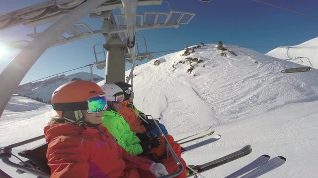 4k footage, four skiing friends sitting on chairlift on sunny winter day
