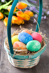 Easter eggs in a basket and tulips on wooden background
