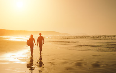 Couple of surfers leaving the water after surfing on a beautiful sunset at the beach. Body board and surf lifestyle concept.