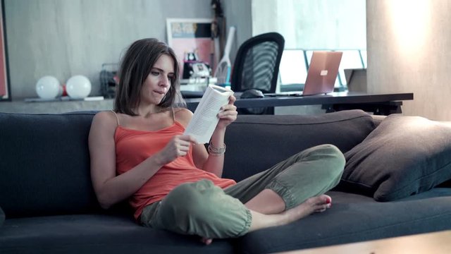 Young woman reading newspaper on sofa at home, 4K
