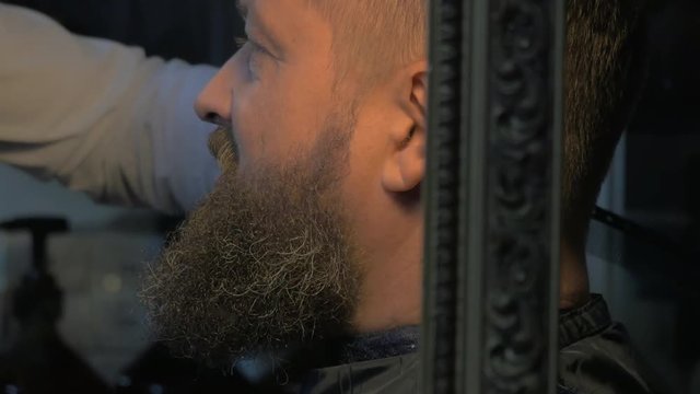 Close up view of female barber taking cares of lush beard of white olded man