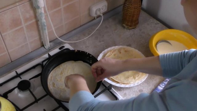 The cook takes from the frying pan pancake and flips it. Then wipes his hands on a towel