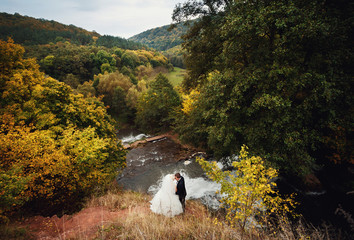 Fototapeta premium Beautiful stylish newlyweds posing near the river outside