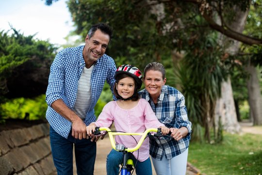happy parents assisting daughter to ride bicycle 