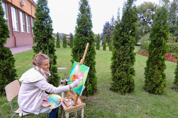 Professional artist woman writes picture sitting at easel with b