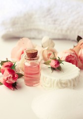 Fototapeta na wymiar Rose aroma attar, white soap bar with foam, fresh pink garden flowers. Botanical skincare and aromatherapy. Vertical. Toned. 