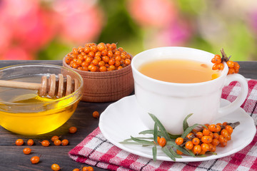 Tea of sea-buckthorn berries with honey on wooden table blurred