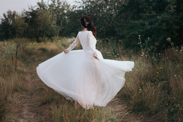 Fototapeta na wymiar Yong bride spinning in a white dress on the bank on nature.Dress develops in the wind. Happy bride in a wedding dress is spinning.