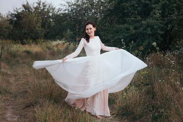 Fototapeta na wymiar Yong bride spinning in a white dress on the bank on nature.Dress develops in the wind. Happy bride in a wedding dress is spinning.
