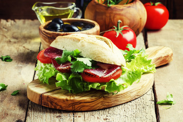 Sandwich with ham, lettuce and tomato in wheat bun, vintage wood