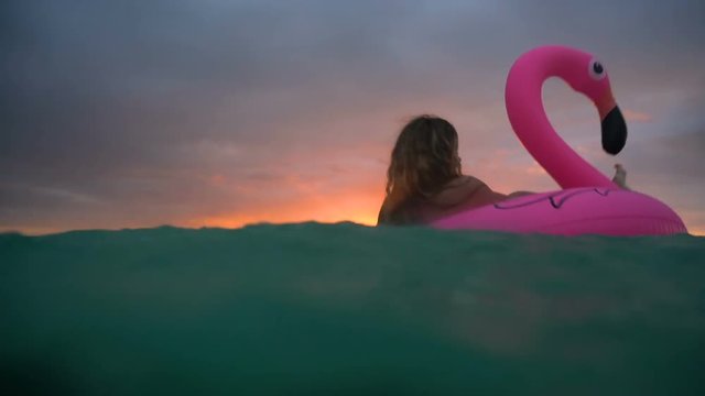 Beautiful girl swimming inflatable flamingo in middle of ocean with a beautiful sunset