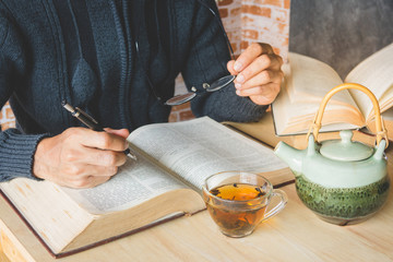 A man reading book with a cup of tea and old book on table