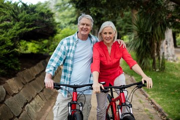 Portrait of senior couple standing with bicycle in park