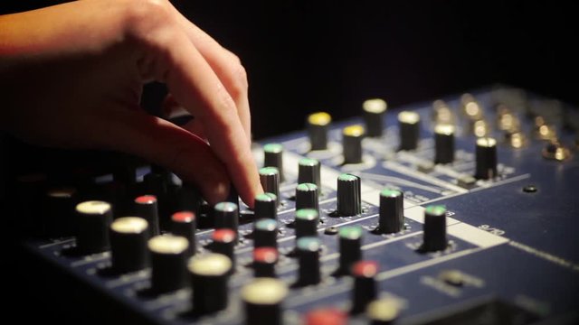 Close up dolly shot of a mixer desk with many buttons and cables, and a hand making adjustments.