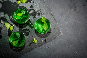 Sweet refreshing mint liqueur, with ice and mint leaves on the slate tray to feed on gray concrete...