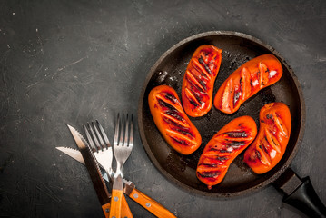 Grilled sausages, homemade, in a pan, on a concrete gray stone table, top view. With ketchup and spices (pepper), copy space