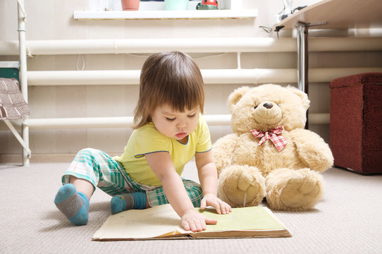 little girl reading book indoor in her room on carpet with toy Teddy bear, cute child playing school, children education and development, happy childhood