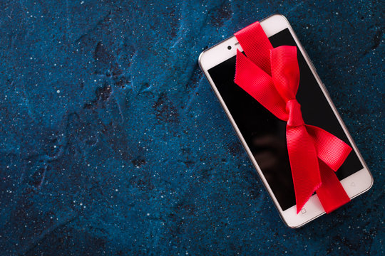 Modern mobile phone decorated with a red ribbon on a dark blue background. Birthday,christmas,valentine day gift concept