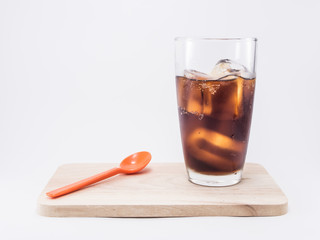 two of thirds soft drink is cool and ice cubes in glass near orange spoon on wood squares