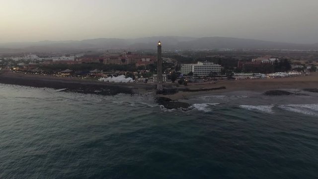 Aerial shot of the Gran Canaria resort and Maspalomas Lighthouse in the evening. Flying from the ocean to the beach