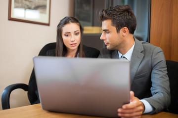 Smiling business people using a laptop computer in their office
