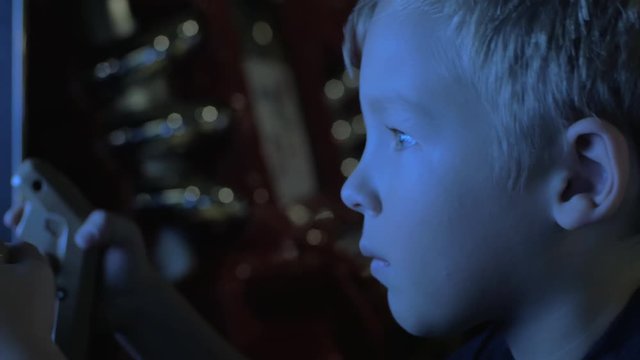 Boy playing shooter on arcade machine. He pushing button on weapon simulator and looking at the screen