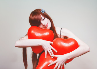 Chica joven y pelirroja abrazando globos rojos con forma de corazón 