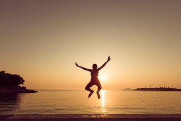 Fototapeta premium Child little girl is jumping into the sea from a pier at sunset