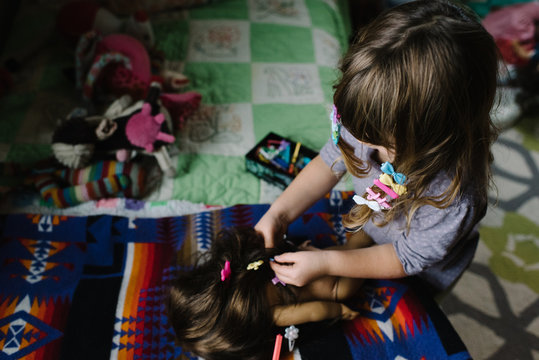 Young girl with hair clips in hair, playing in bedroom, putting hair clips in dolll's hair,