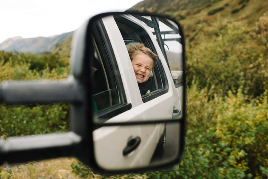 Reflection of a boy in wing mirror while looking out of a car window