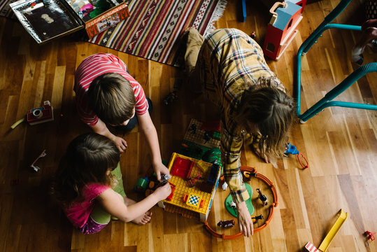 Three children at home, sitting on floor, playing with toys