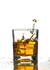 Splash in glass of whiskey and ice isolated on white background wet table