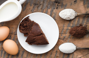 Cake, flour, sugar, cocoa, milk and eggs on a wooden table. Ingredients for cooking.