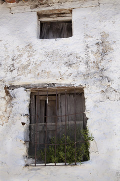 Viejas ventanas con postigos de madera y rejas oxidadas una pared encalada de blanco con desconchones