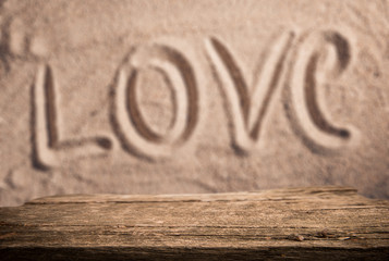 Empty wood table top with love written in sand as Valentines background for display your product