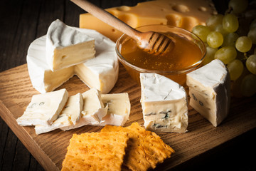 Slate board with various cheese and a glass of red rose wine. Brie. Camembert. Gouda, Masdaam, Roquefort, Cheddar and grapes on a wood with nuts, honey, crackers, blue cheese. Italian, French cheese.