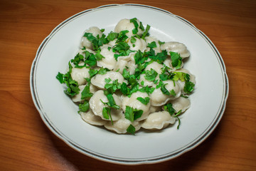 Boiled prepared homemade russian dumplings or pelmeni with beef meat on the white plate with fresh parsley