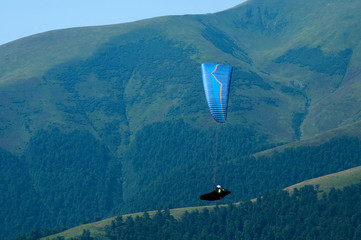 Paragliding in the sky. One paraglider fly over a mountain valley in summer sunny day. Carpathians,...