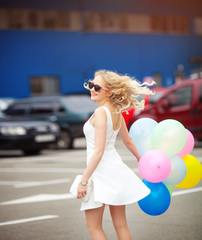 Fototapeta premium Beautiful young blonde with a cheerful mood Dancing in the street with colored balls.