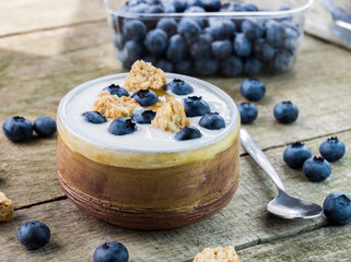 White yogurt with blueberries on the top in bowl on natural wood