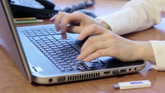 Woman using laptop and inserting USB flash drive. Young businesswoman typing on the keyboard and using white usb flash drive. She inserts it into the modern black laptop.