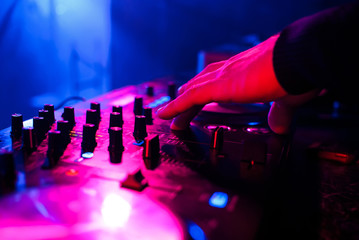 DJ playing on mixer at party on blurred colorful background closeup