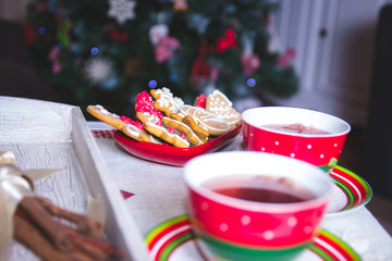 Tasty cookies and cups of tea on a table with a Christmas tree in the background