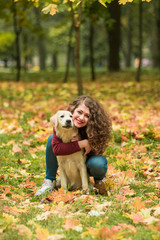 Fototapeta premium Curly woman sitting with her dog in autumn leaves outdoors